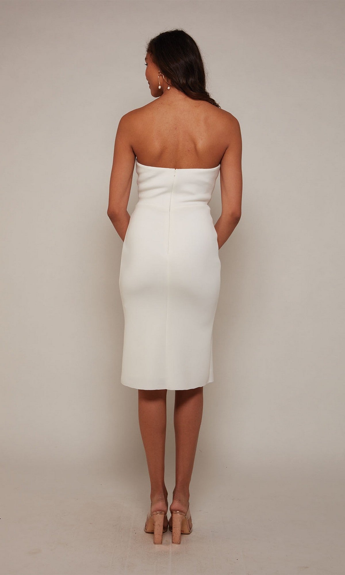 A woman faces away against a light background, wearing the Knee Length White Party Dress: Alyce 70048 and beige heeled sandals.